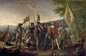 Painting of Christopher Columbus landing in the New World. He and his soldiers raise Spanish flags, while Native Americans bow in fear.