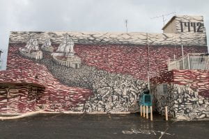 Mural on outside of building in San Juan showing Columbus' three ships sailing away from the New World through a red sea of blood, leaving bodies in their wake