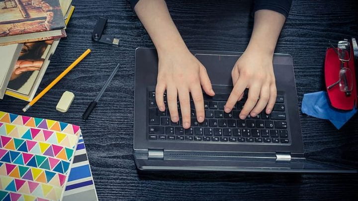 Image of hands typing on laptop next to colorful notebooks