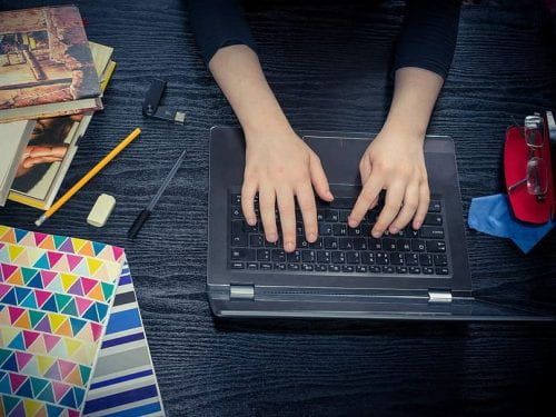 Image of hands typing on laptop next to colorful notebooks